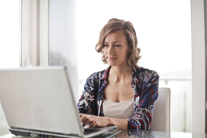 A woman sitting alone in front of her laptop with a serious expression.typing on the keyboard.