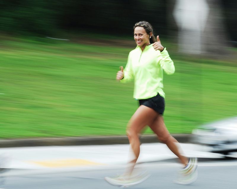 A woman running on a road while giving the thumbs up.