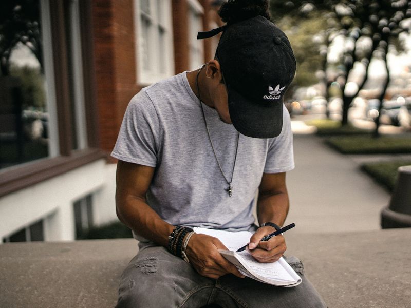 A man writing in a notebook, sitting outside