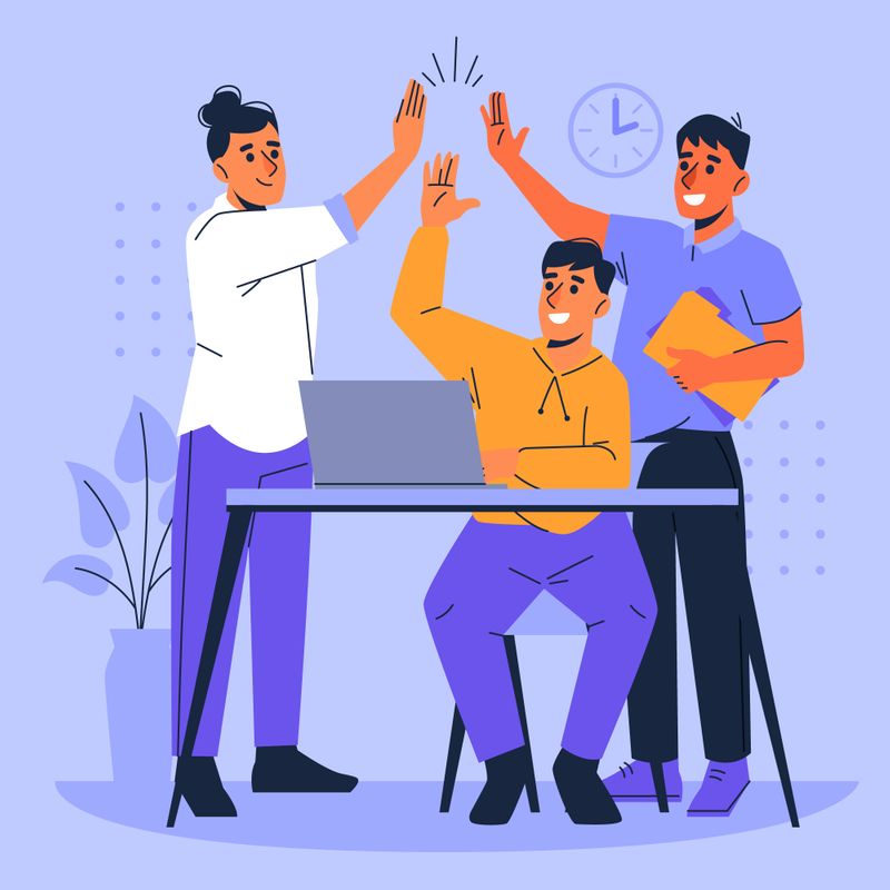 Three people around a desk with a laptop, all high-fiving each other.