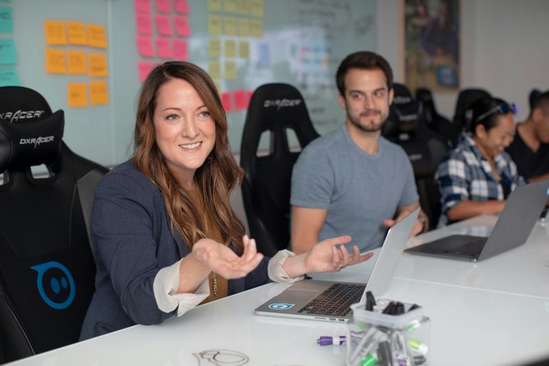 Two people sitting in front of laptops. One is using her hands as she says something.