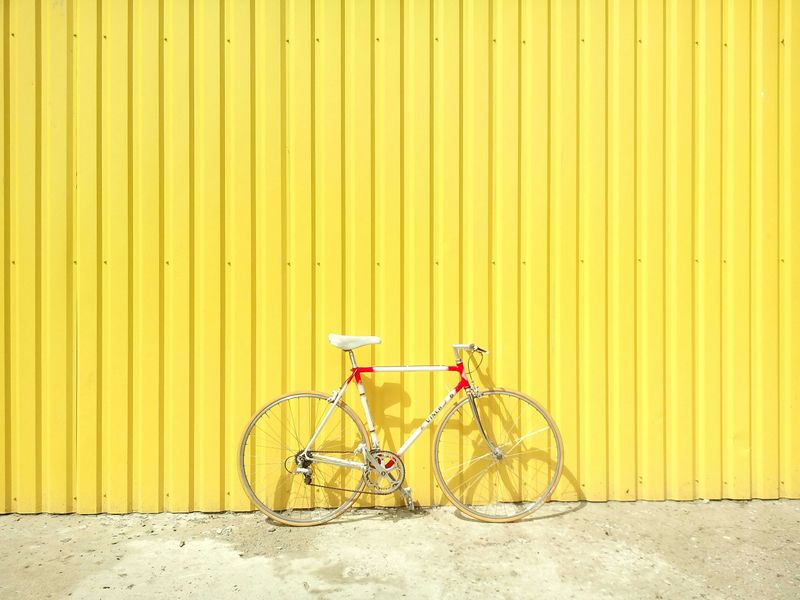 A bike parked on concrete in front of a yellow wall.