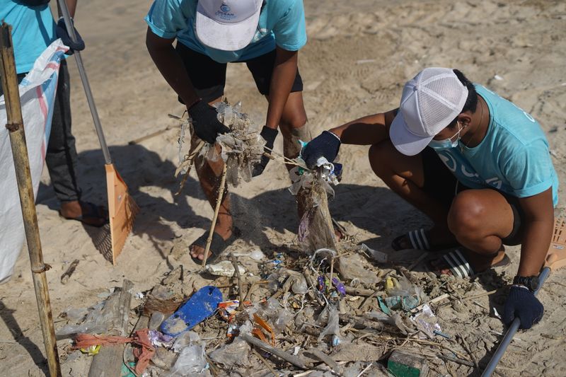 Three volunteers cleaning up beach trash together.