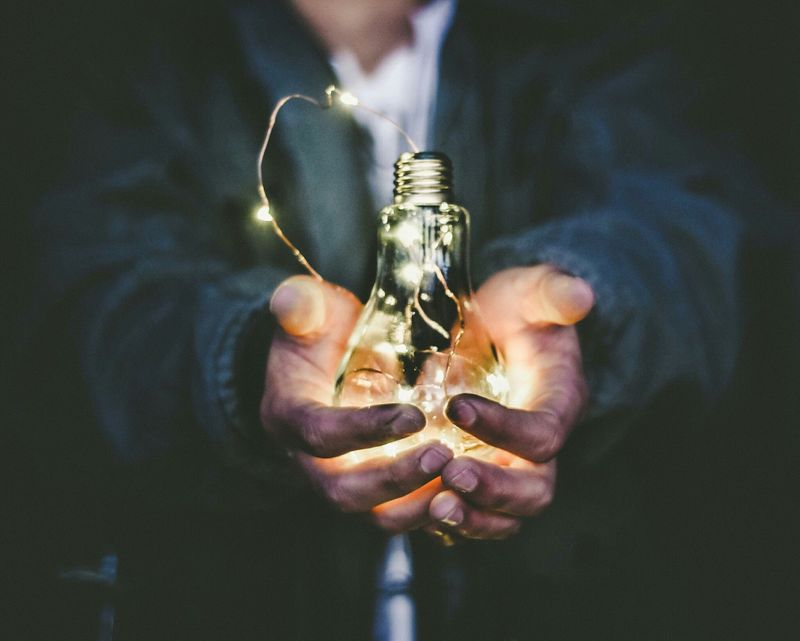 Hands holding a light bulb with small, bright lights inside it. 