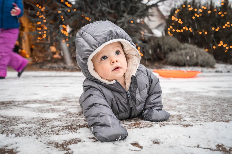 A baby crawls on snow ground while wearing a hooded winter onesie.