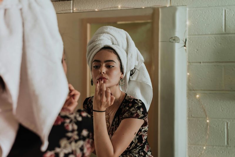 A girl with hair towel on her head applying lipstick with her finger