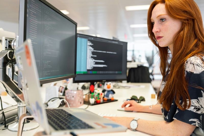 A woman with two computer screens and a laptop open in front of her. 