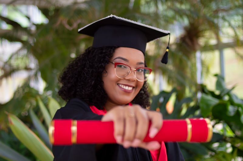 A black woman smiling and holding a red and gold diploma canister