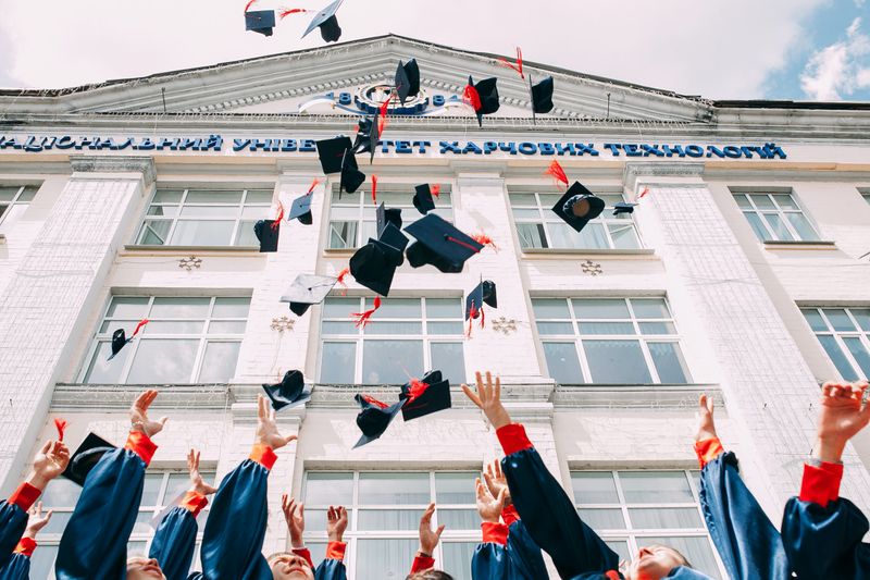 Hands tossing graduation hats in front of a school.