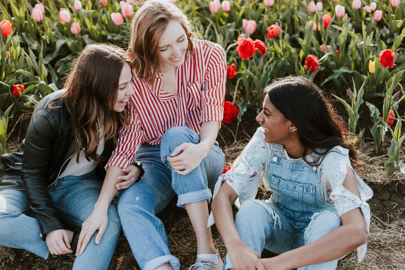 Three young women sit surrounded by tulips.