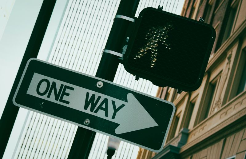 A one way traffic sign below a pedestrian walk signal.