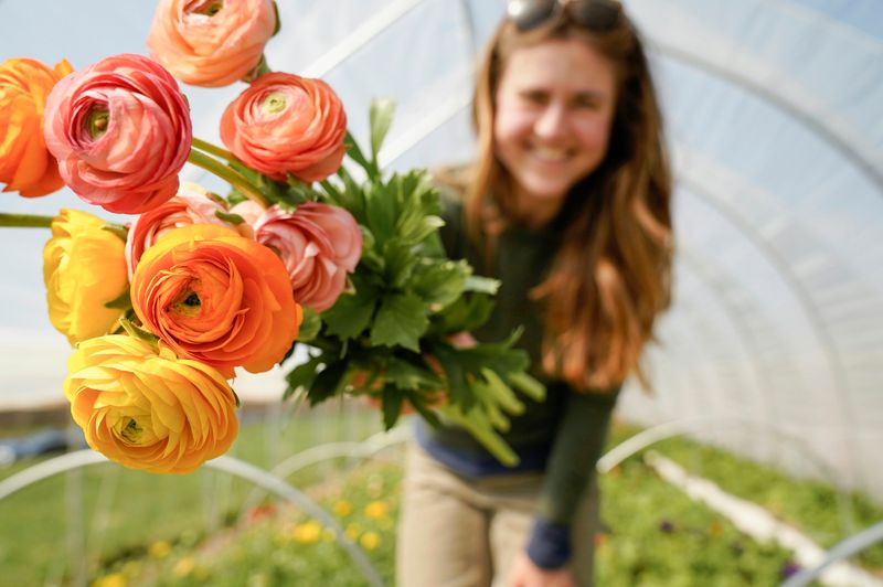 A woman holding out a bouquet of yellow and pink roses.