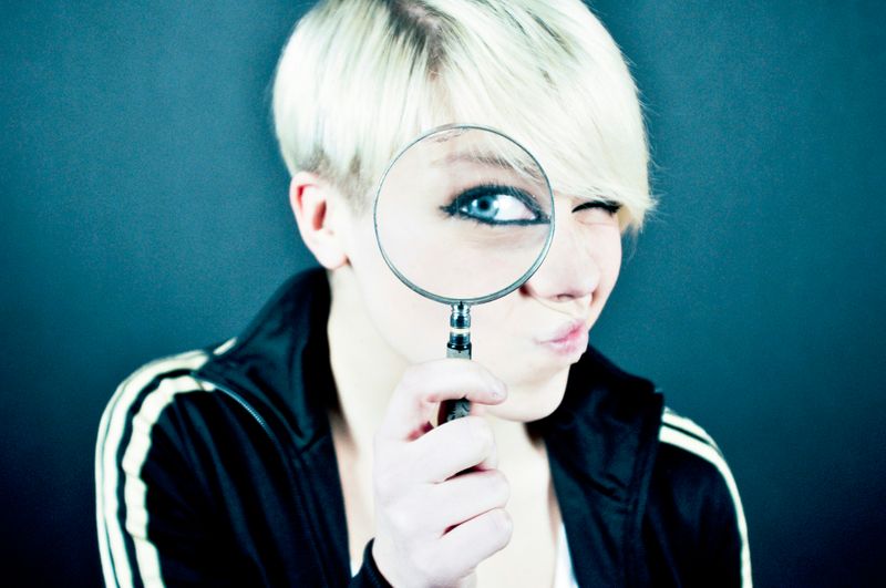 A college age girl looking through magnifying glass.