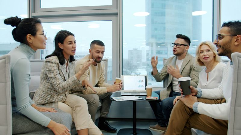 A group of people sitting and talking in group while some holding coffee cups in their hands. 