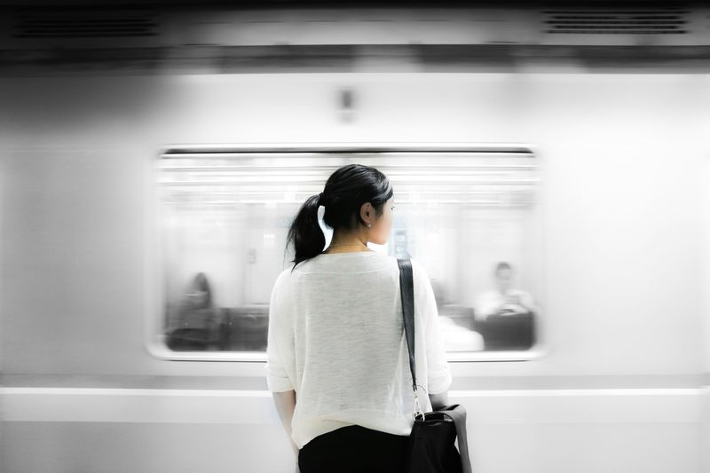 A woman standing and looking to her right, as a train zooms by in front of her.