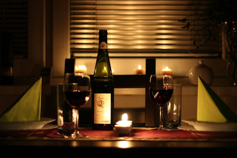 A romantic candle-lit dinner with a bottle of wine and two glasses on a table.