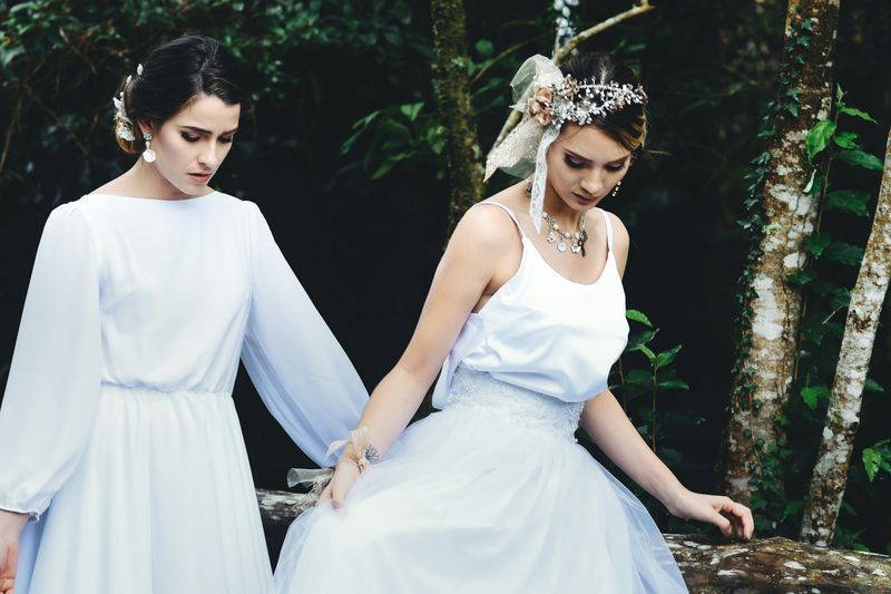 Two women wearing white dresses in a forest.