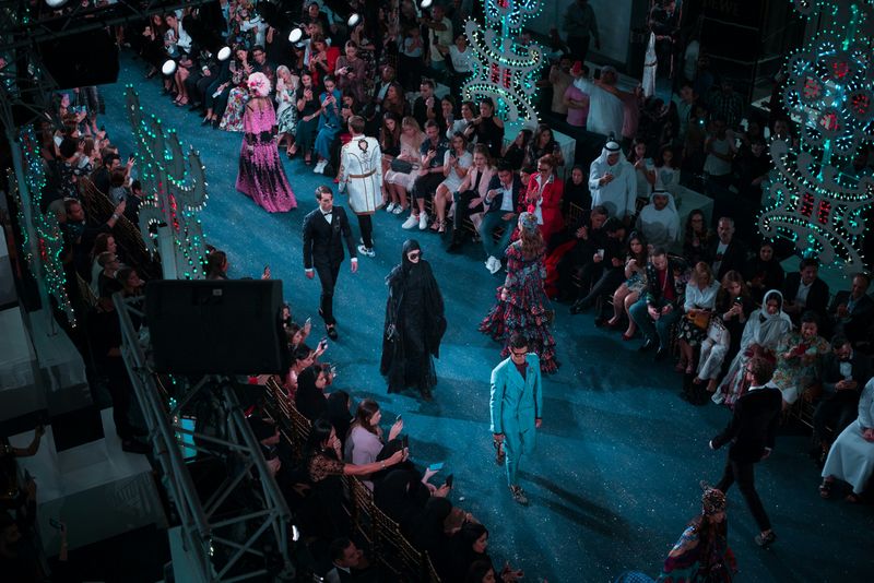 A fashion show with diverse models walking down a runway in fashionable clothes.