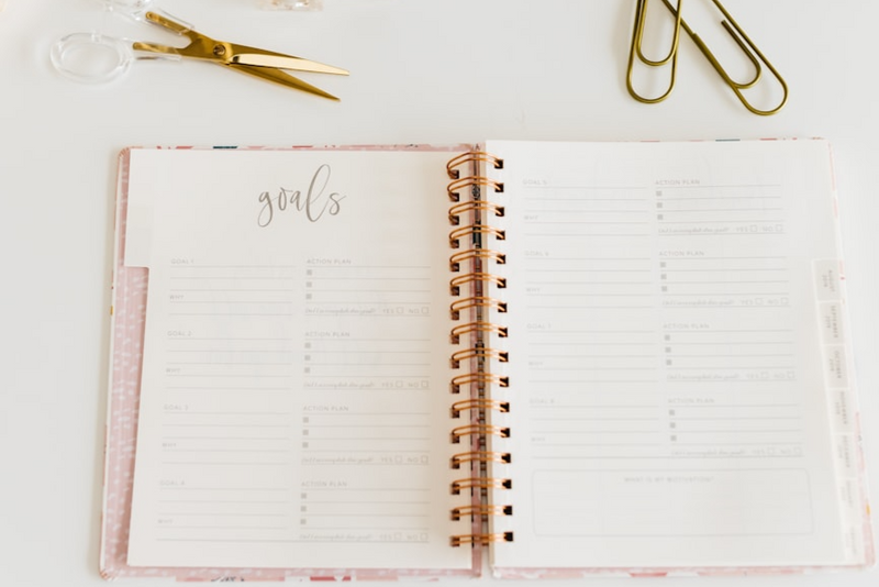 A goals journal on a desk. Some scissors and paper clips are scattered around the journal.