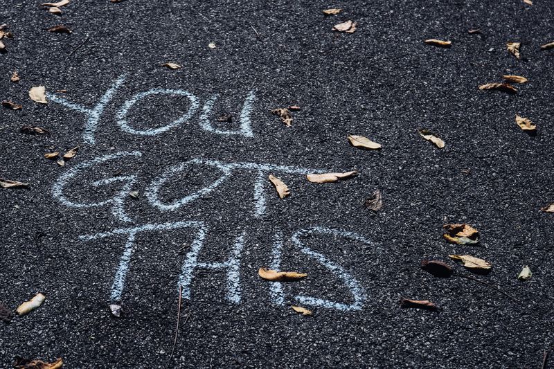 Writing in blue chalk on black asphalt that reads, 'YOU GOT THIS'. 