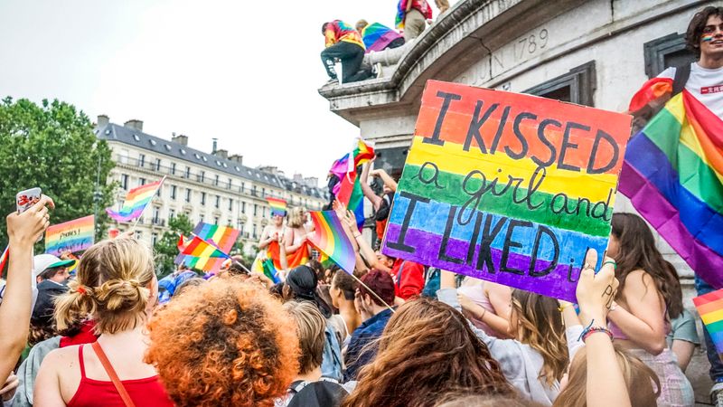 A Pride march. A person holds up a poster that reads, 'I kissed a girl and I liked it.'