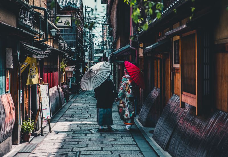 Two women walking with parasols in Japan down a road with traditional buildings