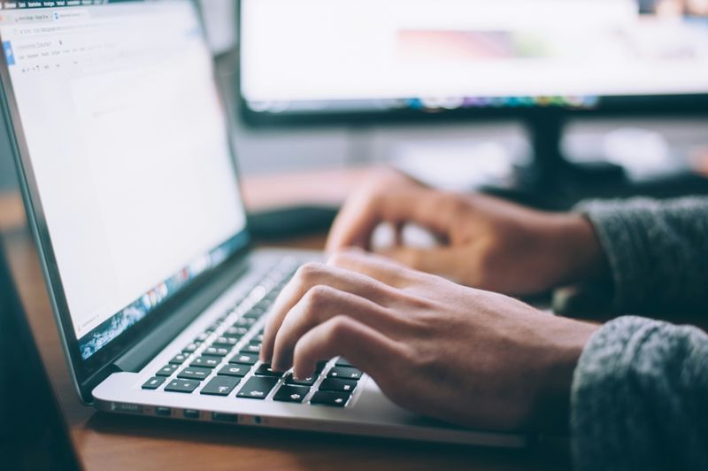 Hands typing a ChatGPT prompt on a laptop.