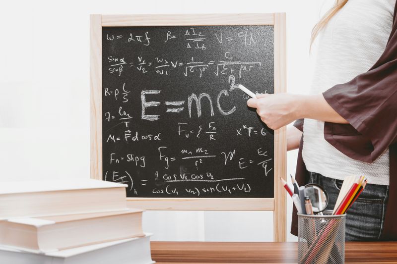 A person pointing at a chalk board of Einstein’s famous equation E = MC^2.