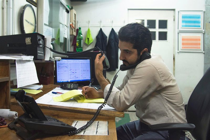 A man talks on the phone while taking notes and multitasking at a busy desk.