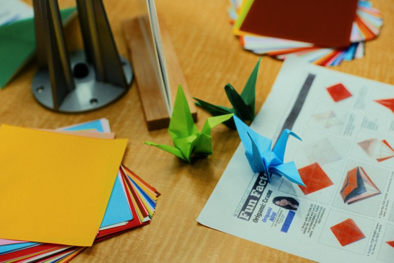 Colorful sheets of origami and two paper cranes on a wooden table.