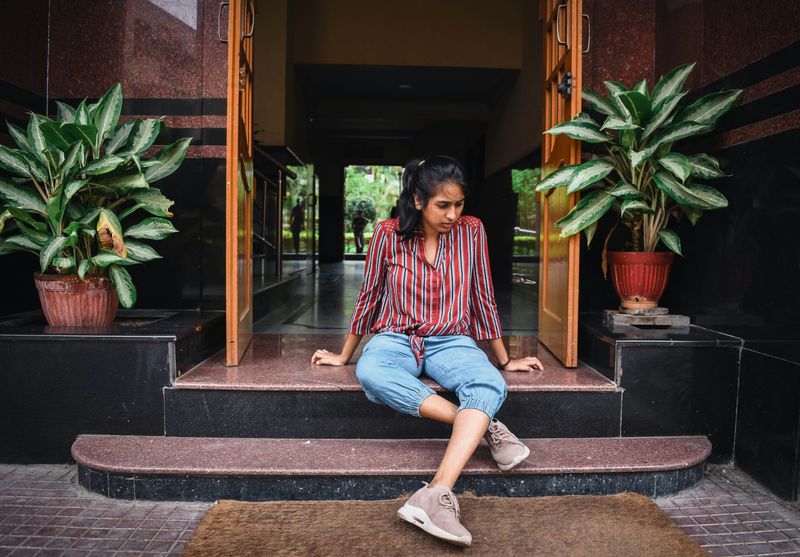 A young woman sitting on outdoor steps, looking down and cradling one leg.