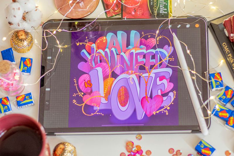 'All you need is love' drawn in colorful calligraphy on a tablet.