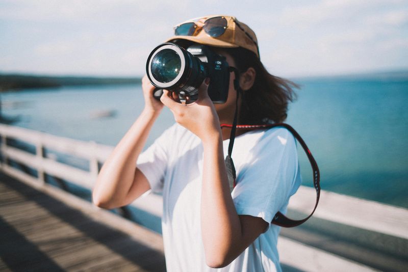 A person on a seaside boardwalk taking a picture with a camera.