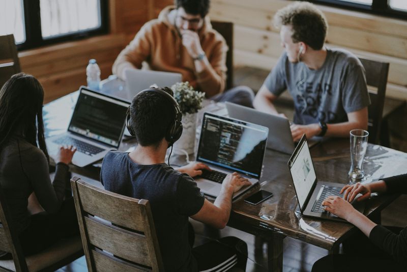People in a meeting. They use their laptops at a table.