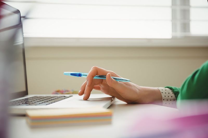 Person working on laptop and holding a pen. 