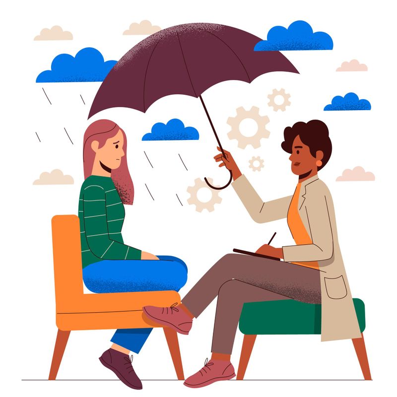 Two people sitting in chairs talking on a rainy day. One person is holding an umbrella and taking notes.