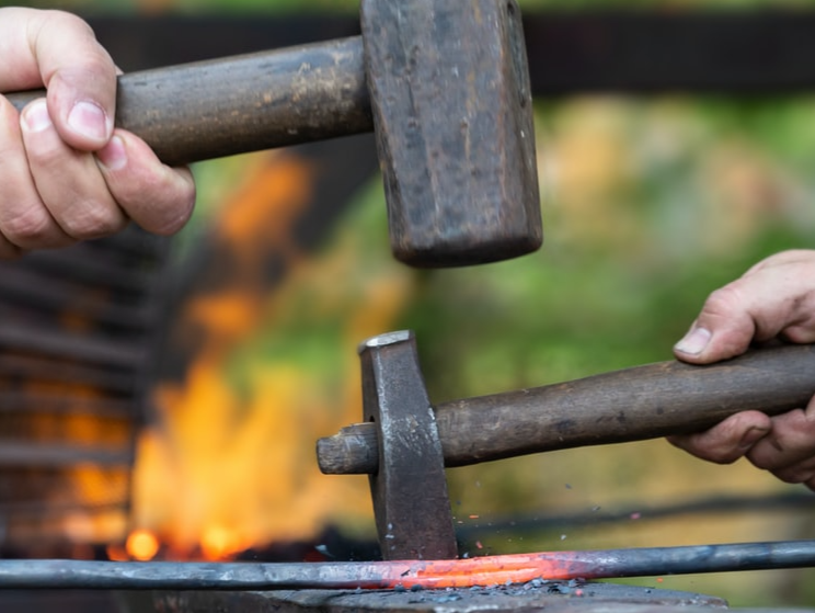 Person using a cross peen hammer for shaping metal.