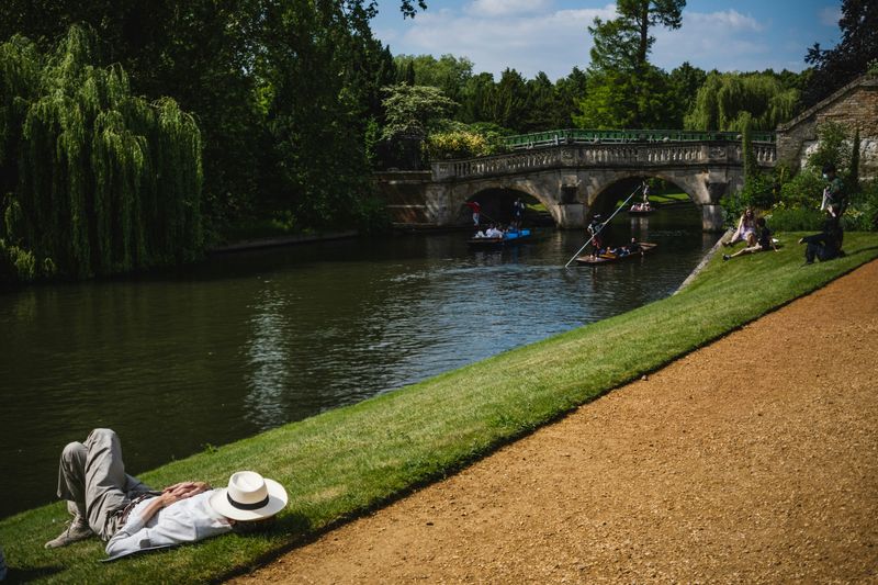 A man lays on the grass by a river with a hat covering his face.