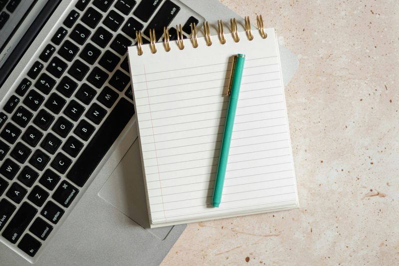 A blank notebook with a green pen resting on a laptop keyboard. 