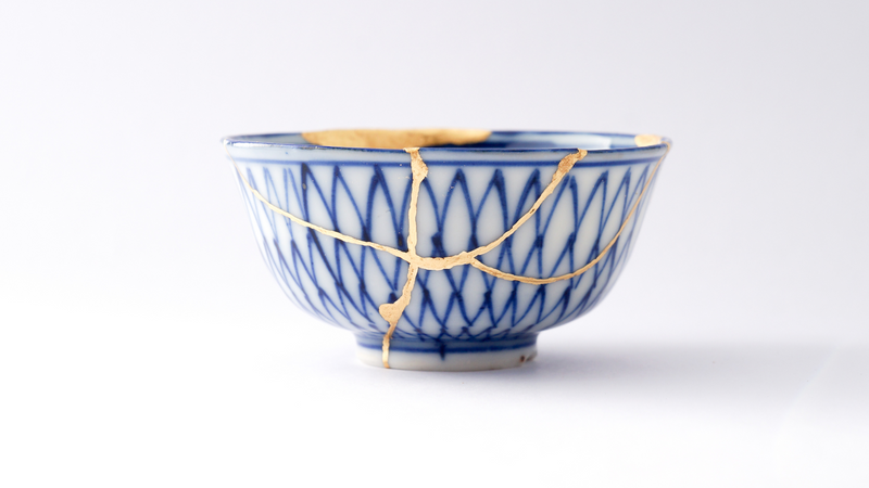 A blue and white ceramic bowl repaired by the Kintsugi method. Golden lines hold the bowl together.