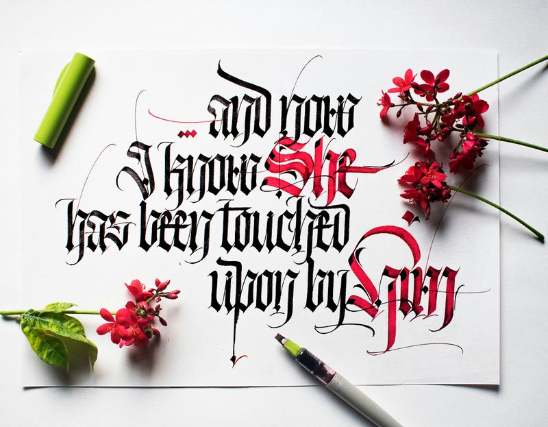 Writing in blackletter script on a white paper sheet, with red flowers strewn around it.