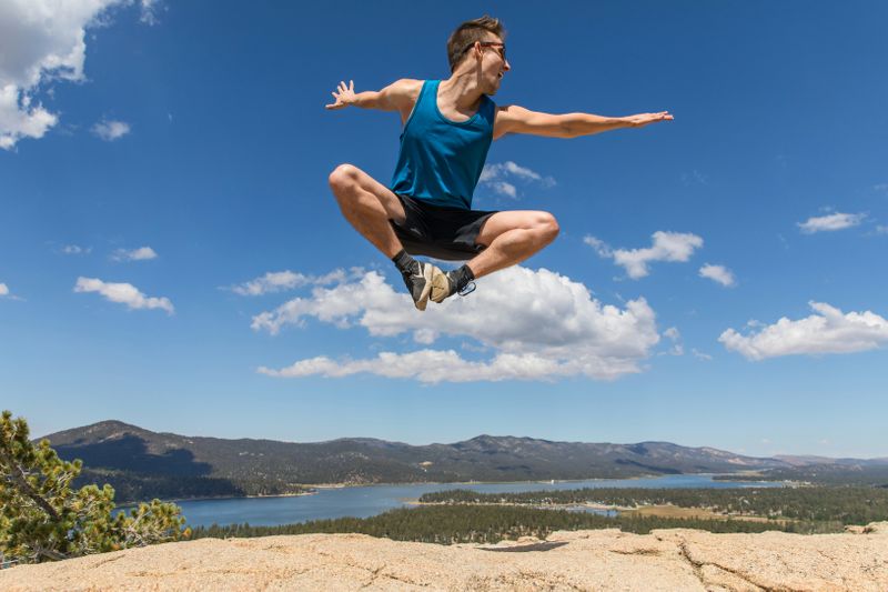 A man jumping in the air with hands and feet up expressing happiness on top of a cliff with a beautiful view.