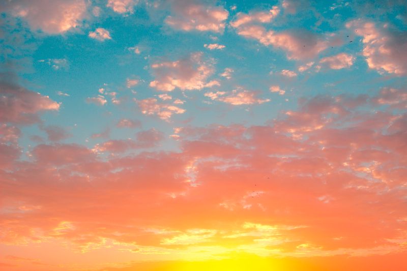 Yellow and orange sunrise with a blue sky and fluffy white clouds.