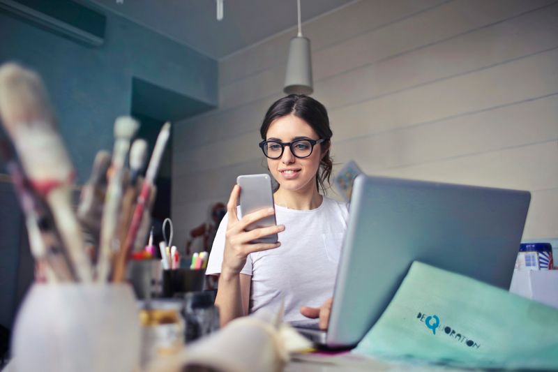 Person sitting at a desk in front of a computer looking at their cellphone