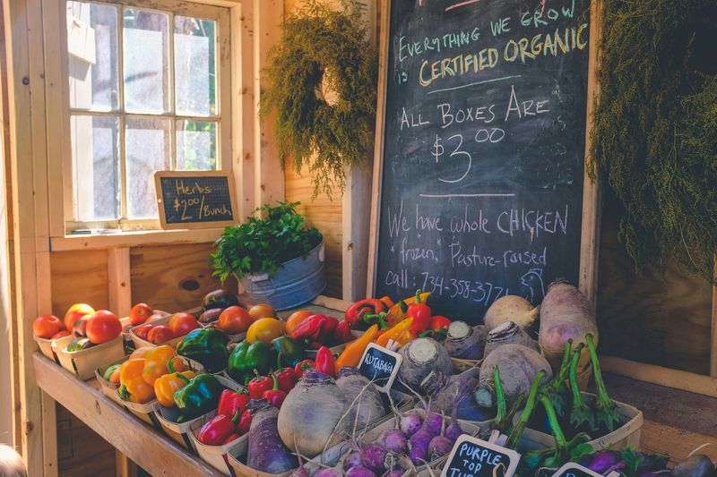 Fruits and vegetables on a wooden shelf in store. A chalk board sign says 