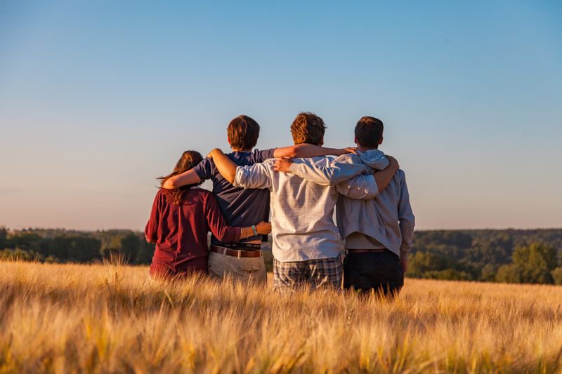 A family standing in a field with their arms on each other's shoulders comforting one another.