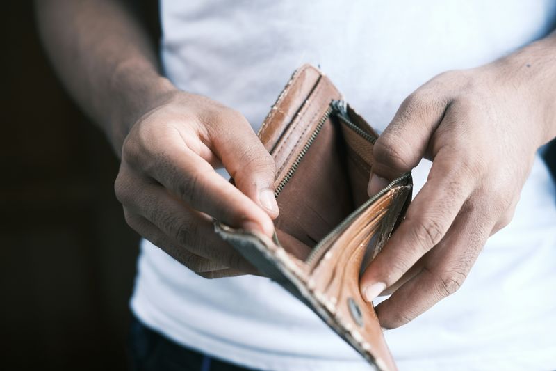 A man holding open an empty brown wallet