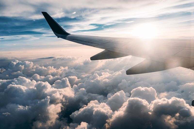 A plane's wing in the clouds with sunlight shining over the sky.