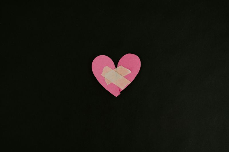 Pink paper heart torn and repaired with adhesive bandages.