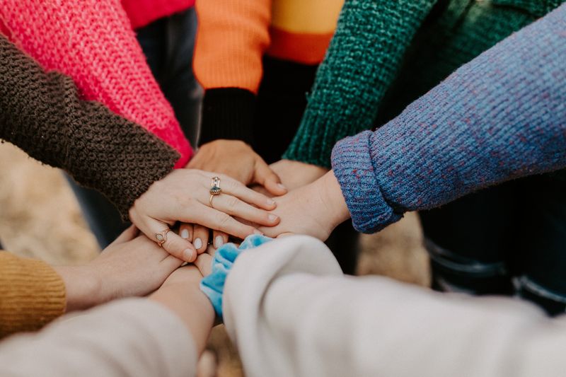 8 women's hands are resting on top of one another, in a huddle.